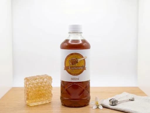 Botella de Miel ½ L de miel artesanal A Cucharadas, junto a un panal y un cucharón de miel