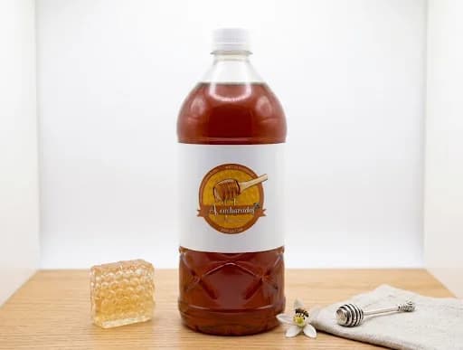 Botella de Miel 1 L de miel artesanal A Cucharadas, junto a un panal y un cucharón de miel